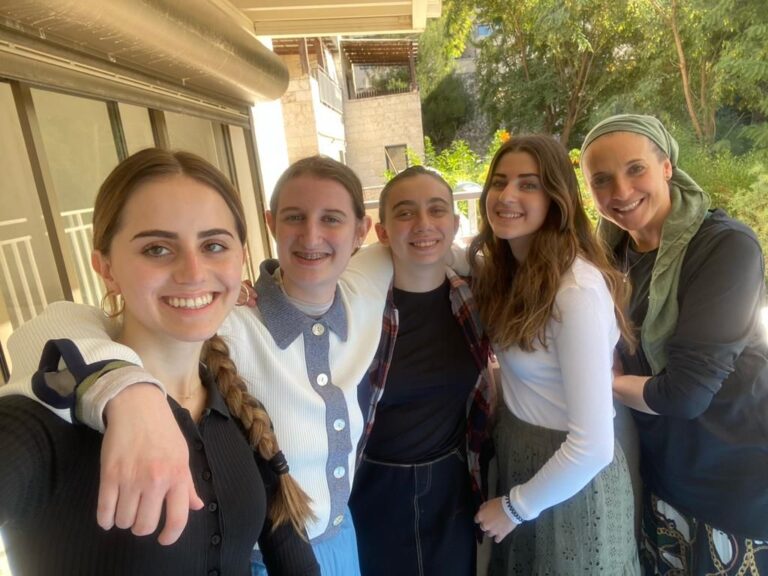 Five smiling women posing together outdoors
