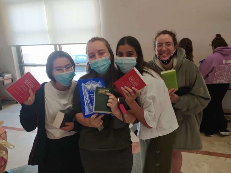 Four masked students holding small colorful books