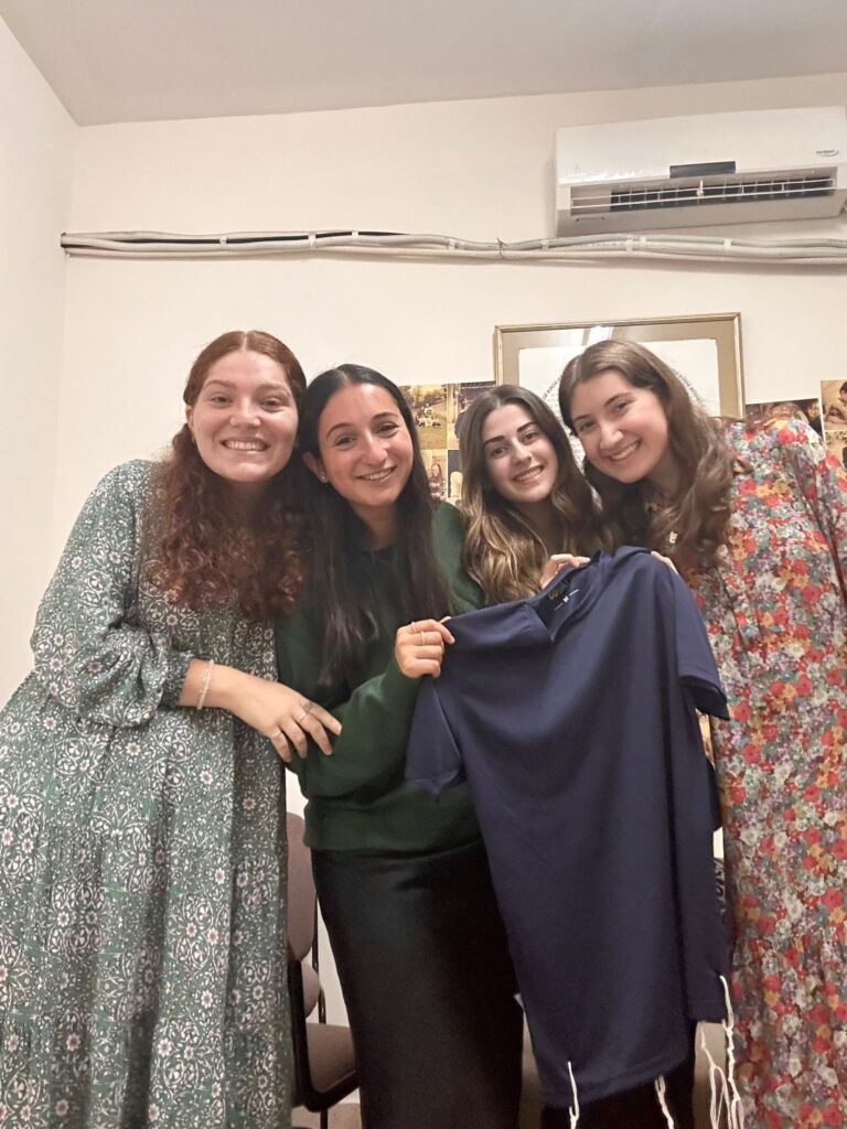Four smiling women holding navy blue shirt