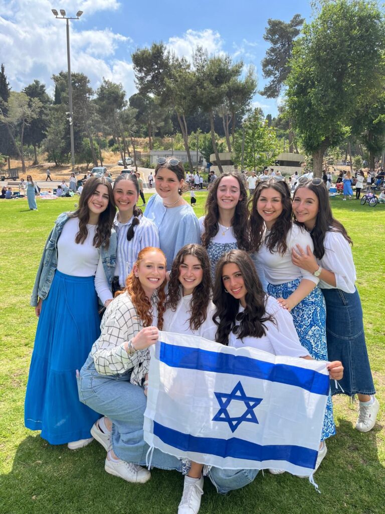 Smiling friends posing outdoors with Israeli flag