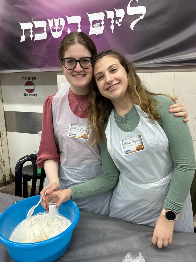 Two smiling women stirring dough in blue bowl
