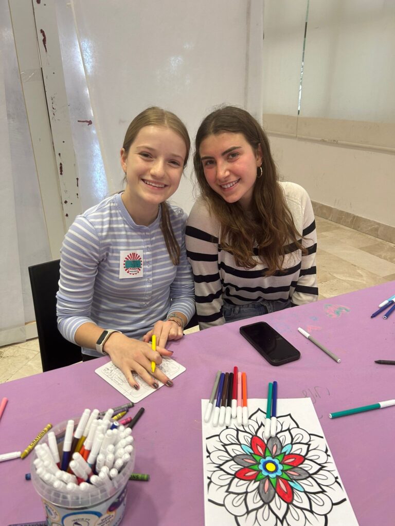 Two smiling girls coloring mandala at table