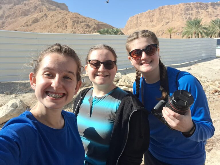 Three smiling people in blue shirts outdoors