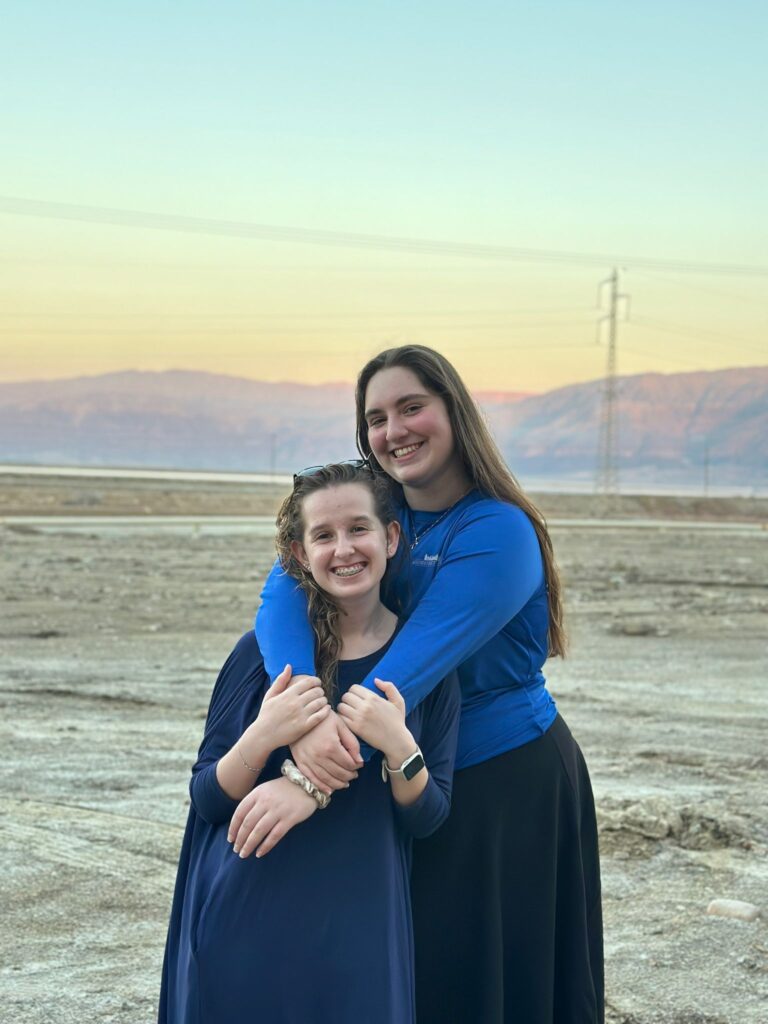 Two smiling women hugging by lakeside sunset