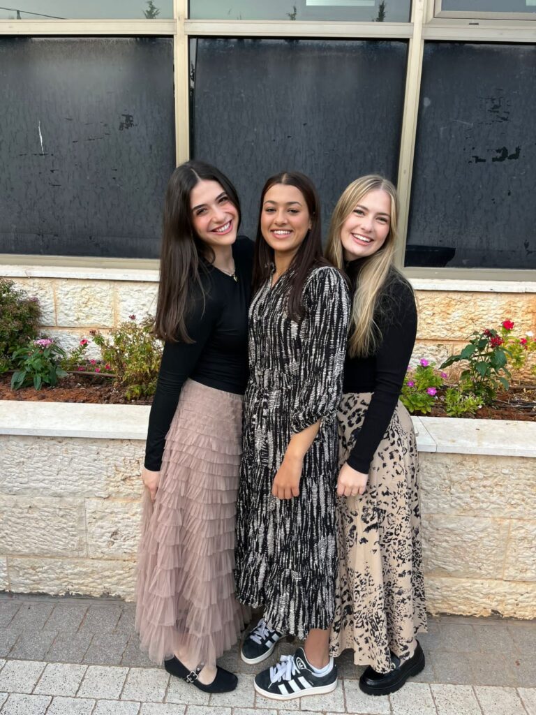 Three smiling women in skirts by flowerbed