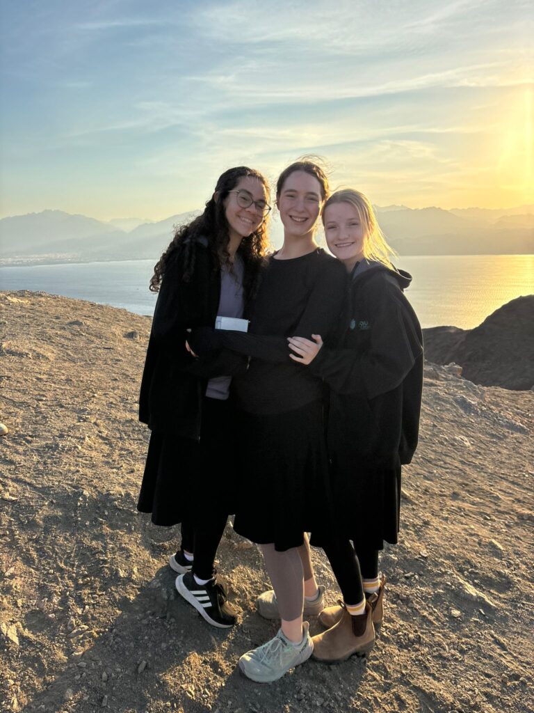 Three friends hugging on coastal cliff at sunset