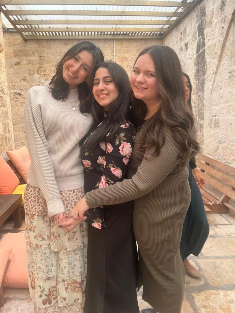 Three smiling women hugging in stone courtyard