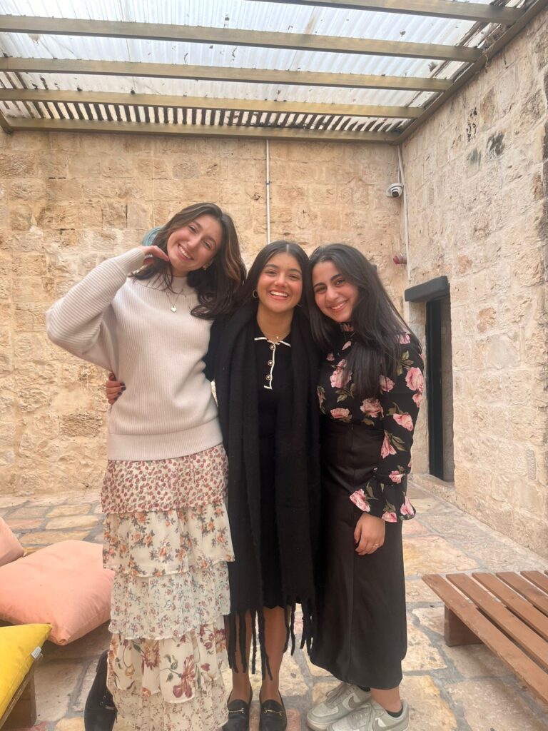 Three smiling women in stone-walled courtyard