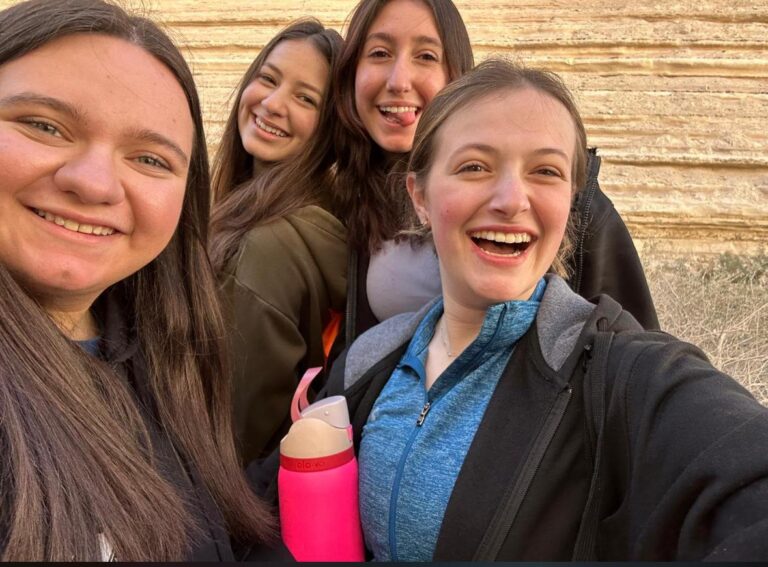 Four friends smiling outdoors taking a selfie