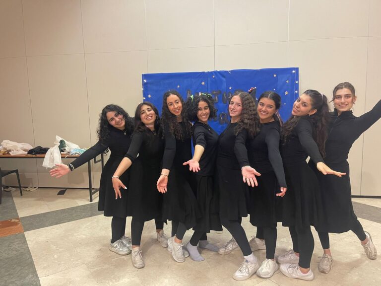 Nine women in black dresses, arms outstretched