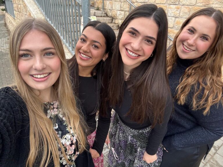 Four smiling young women taking outdoor selfie