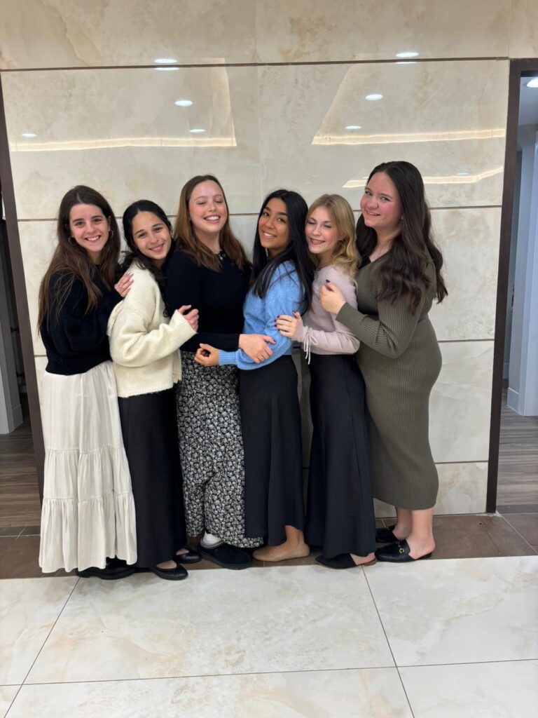 Six smiling women standing closely and hugging