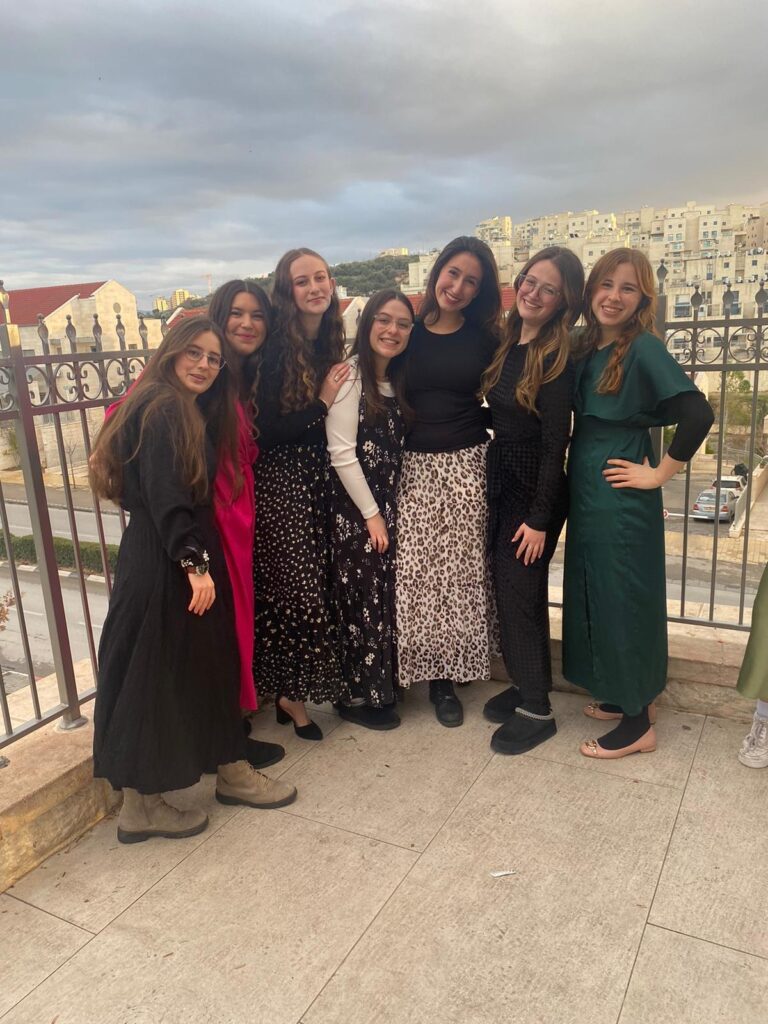 Seven women posing on balcony with cityscape