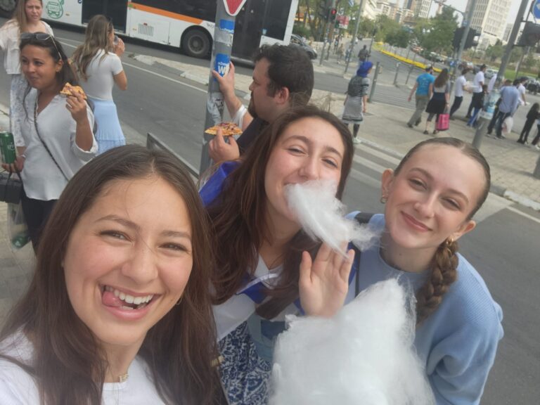Three smiling friends eating cotton candy outdoors