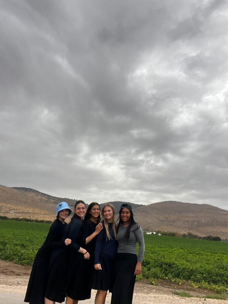 Five women smiling in field under cloudy sky