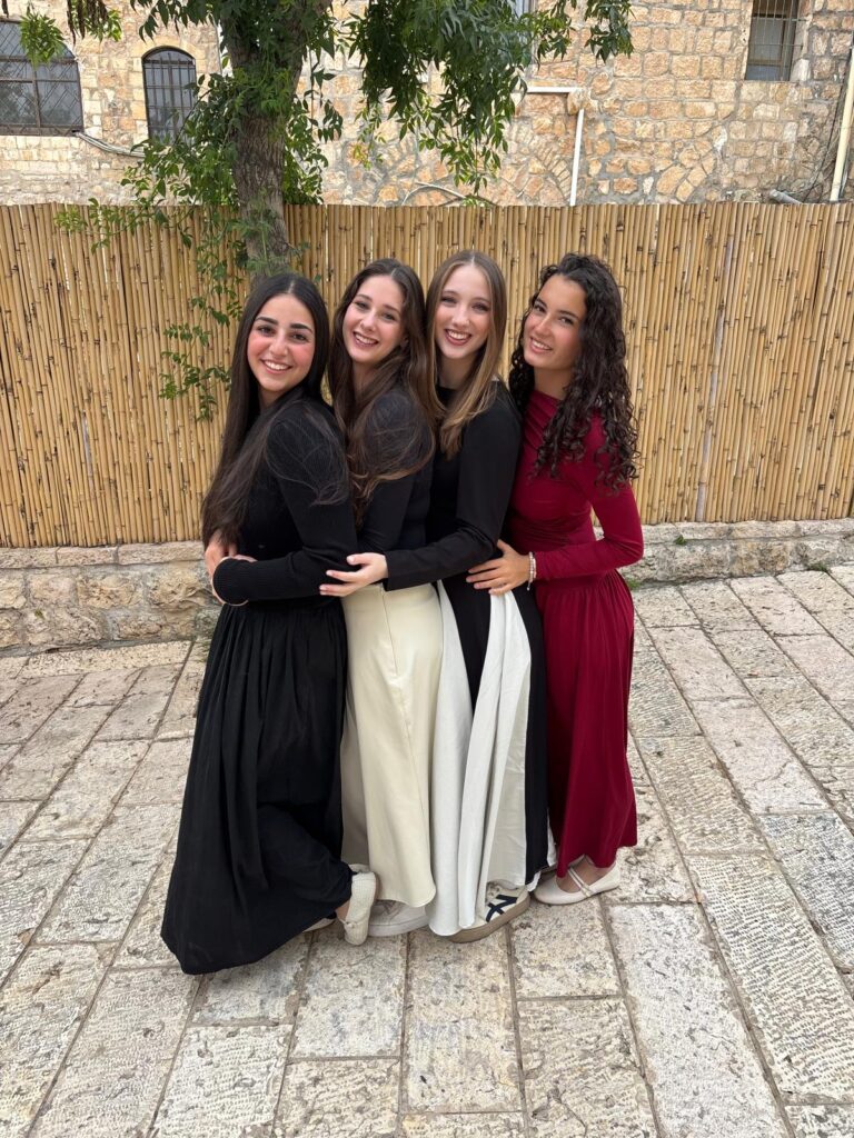 Four smiling women in long dresses hugging
